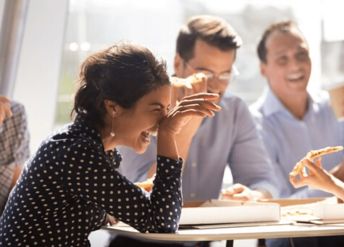 Women laughing while eating lunch with team members in an office