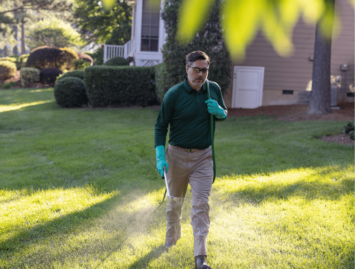 Man spraying chemicals on the lawn of a home on a sunny day