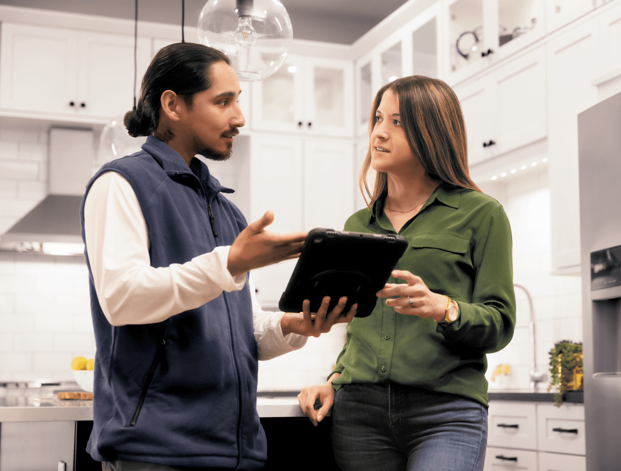 Man and woman in a kitchen talking and referring to tablet