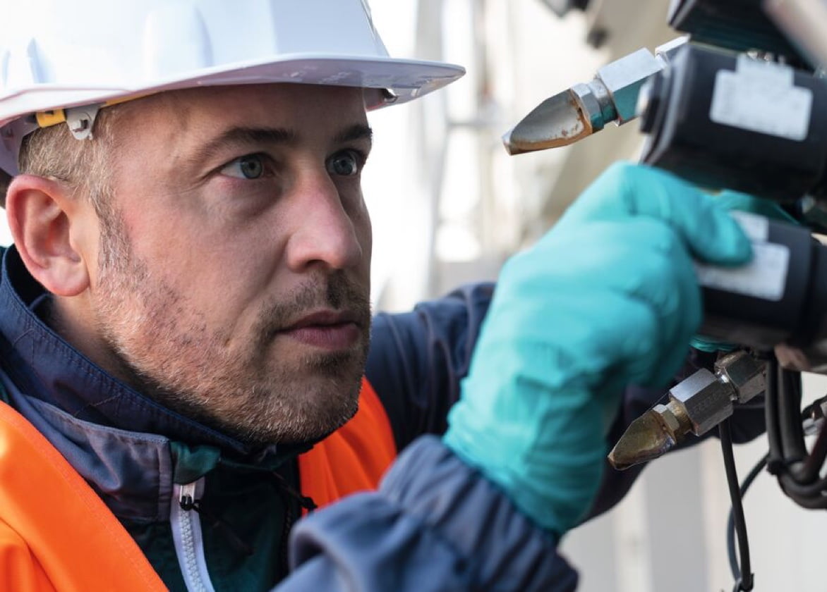 A man wearing a high visibility vest, hard hard, and gloves works with a machine.