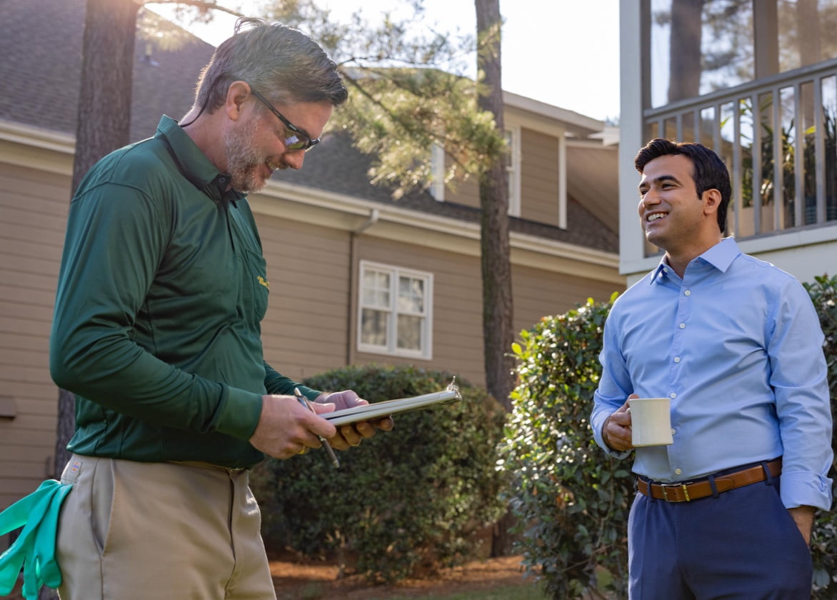 A man holding a coffee mup laughing with a lawn care employee.