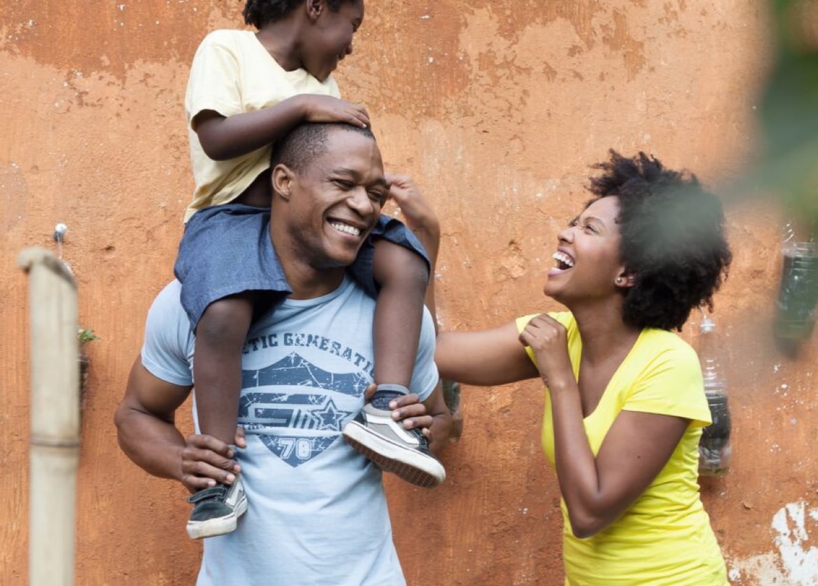 A child sits on a man's shoulders and laughs with him and a woman.