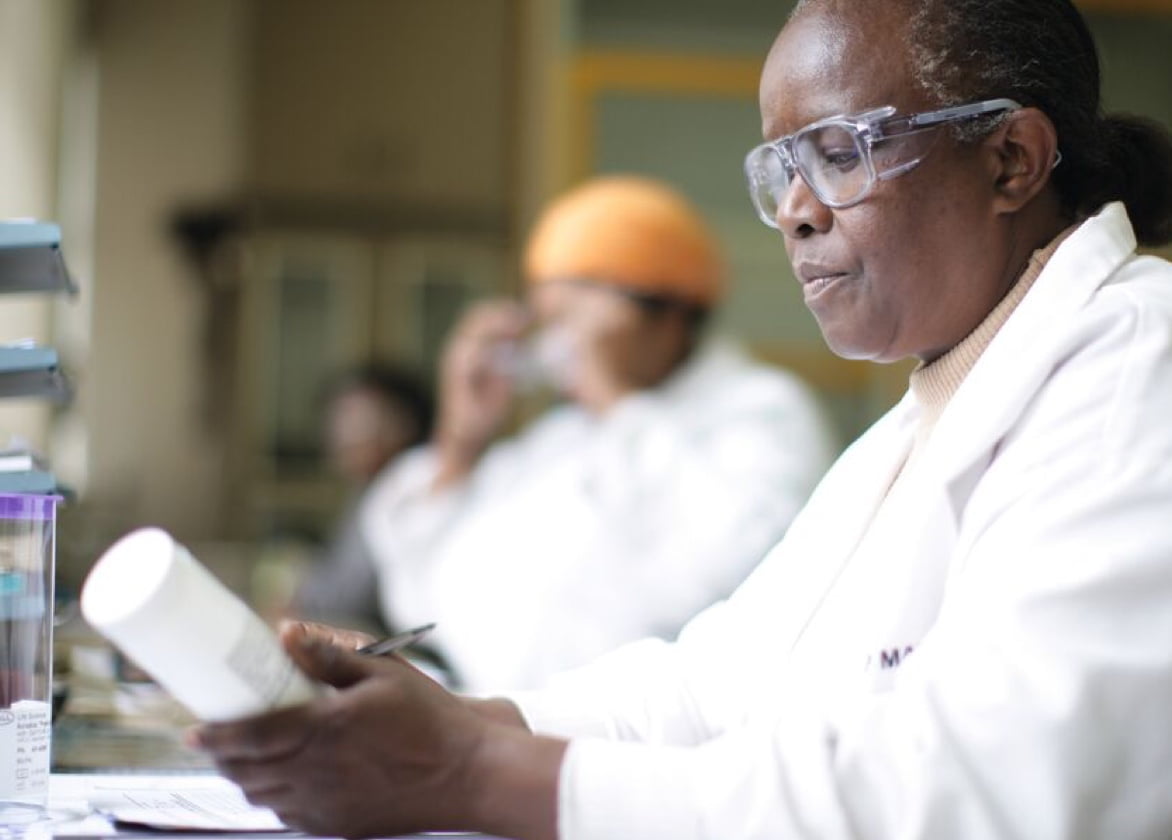 A scientist in a lab coat and safety glasses inspects a product.