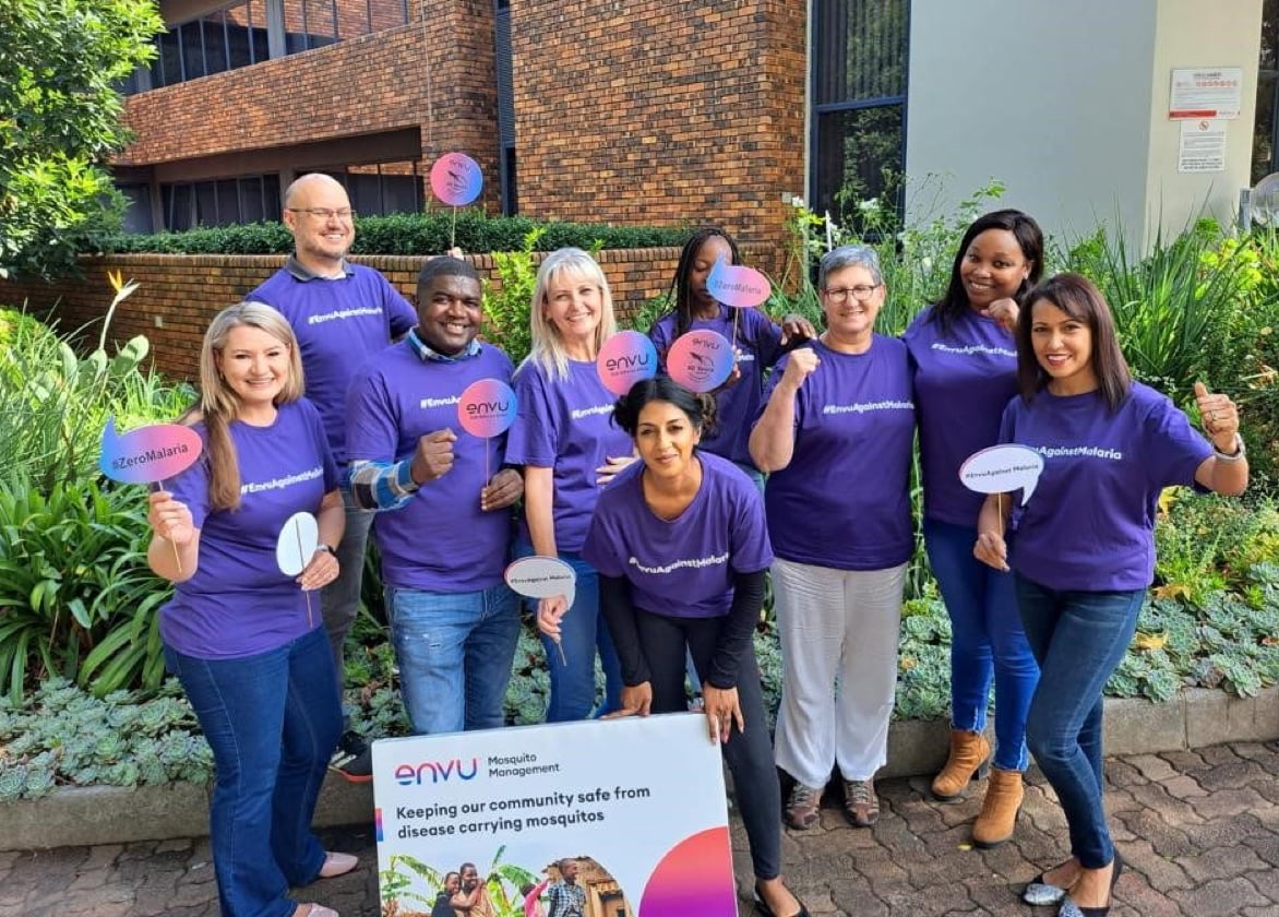 A diverse group of people wearing purple Envu shirts hold branded props and smile.