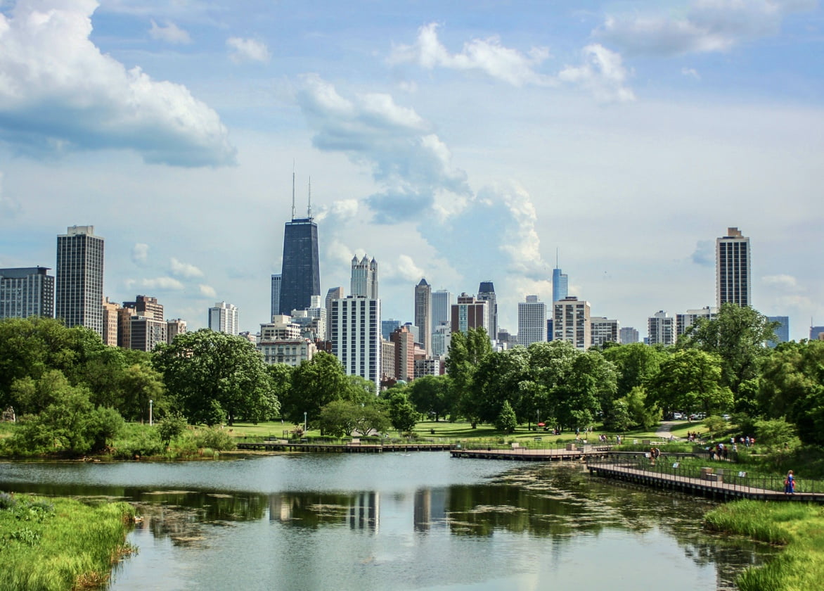 A view of lush landscaping surrounding a body of water and a city skyline in the distance.