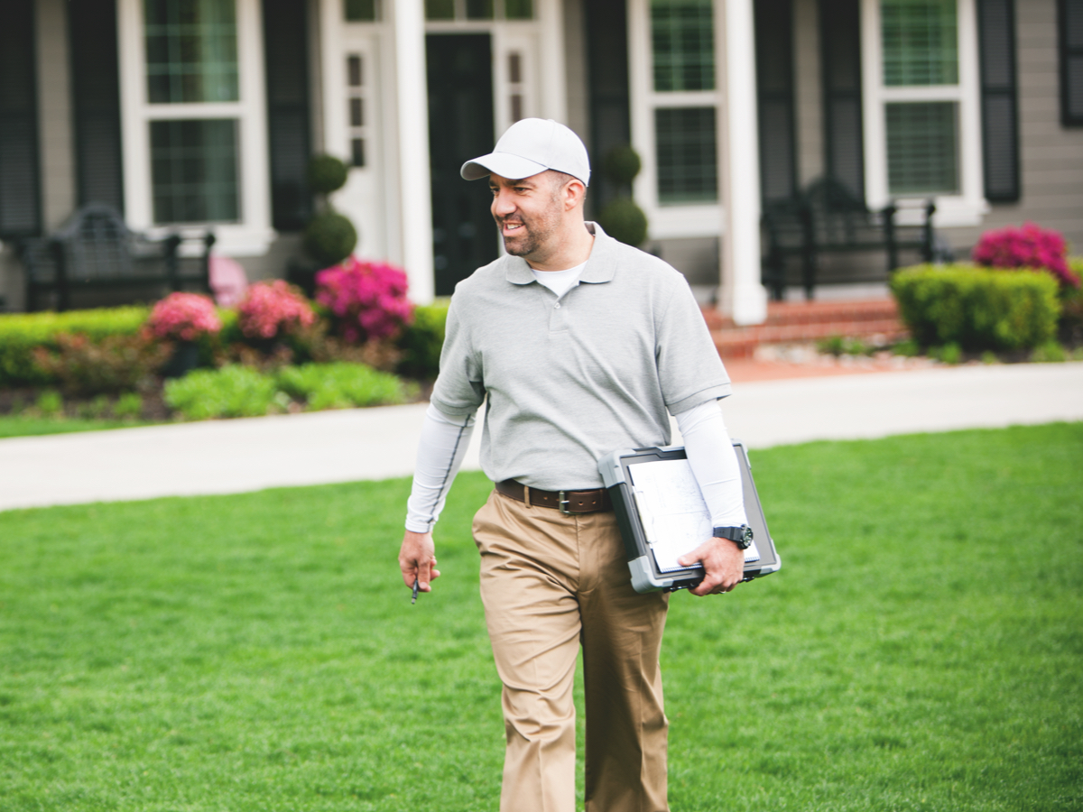 man with laptop under his arm walking across a lawm