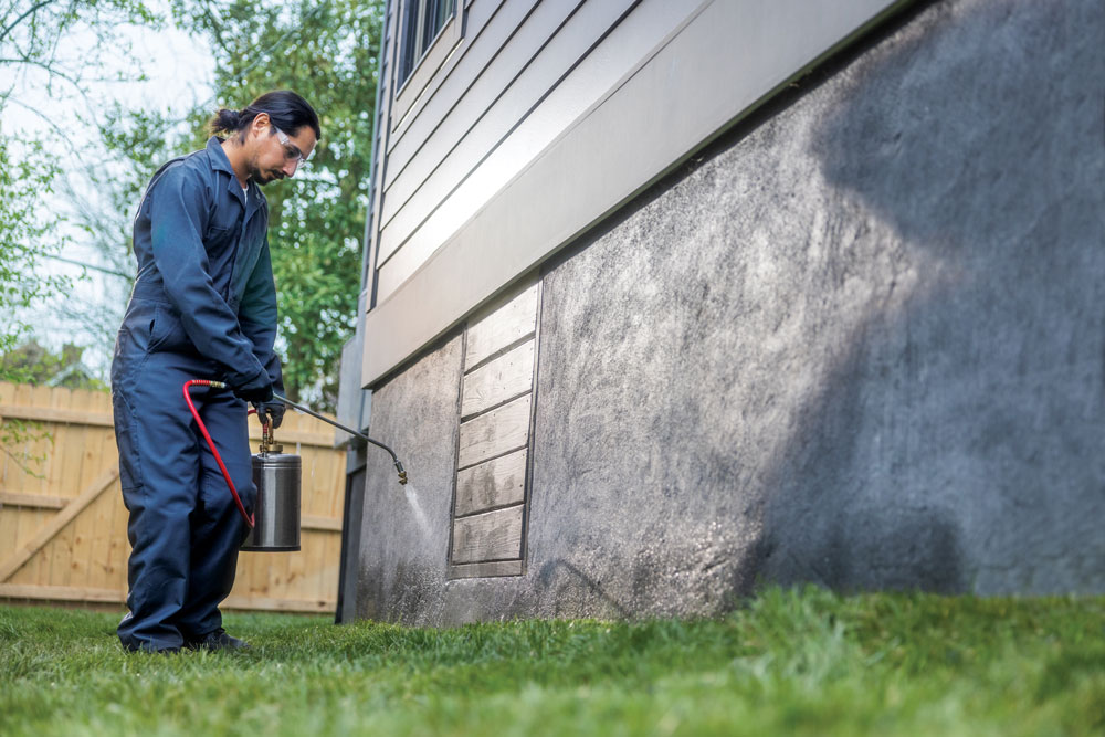 sprayer operator applying product near base of home