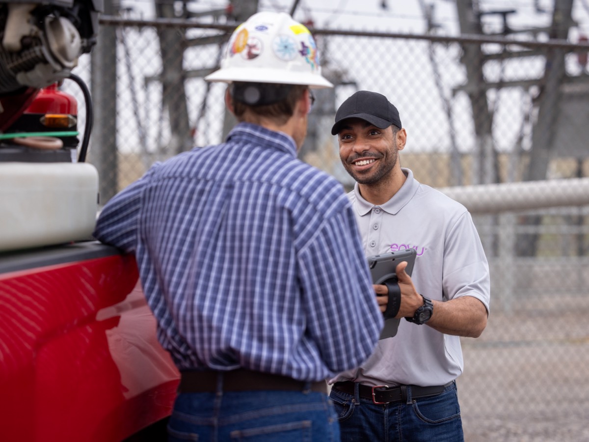 man wearing hard hat leaning on red truck talking to man holding tablet