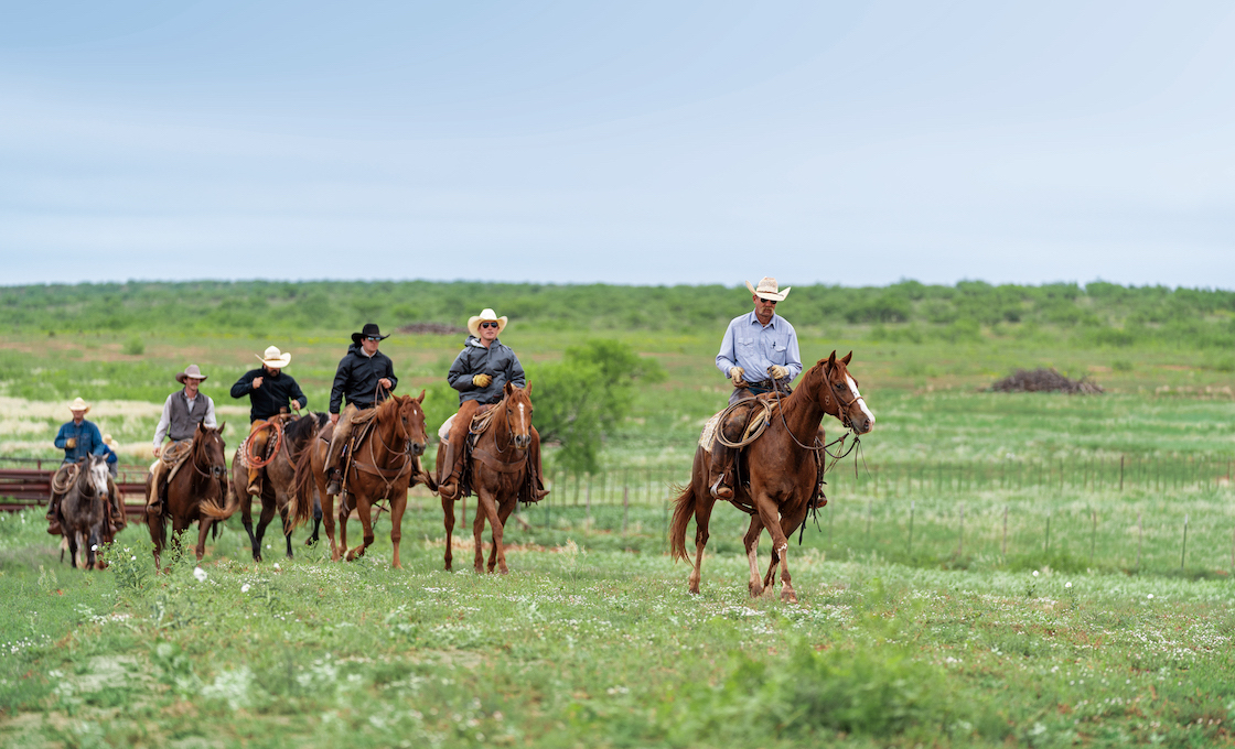 ranchers on horseback riding through pasture